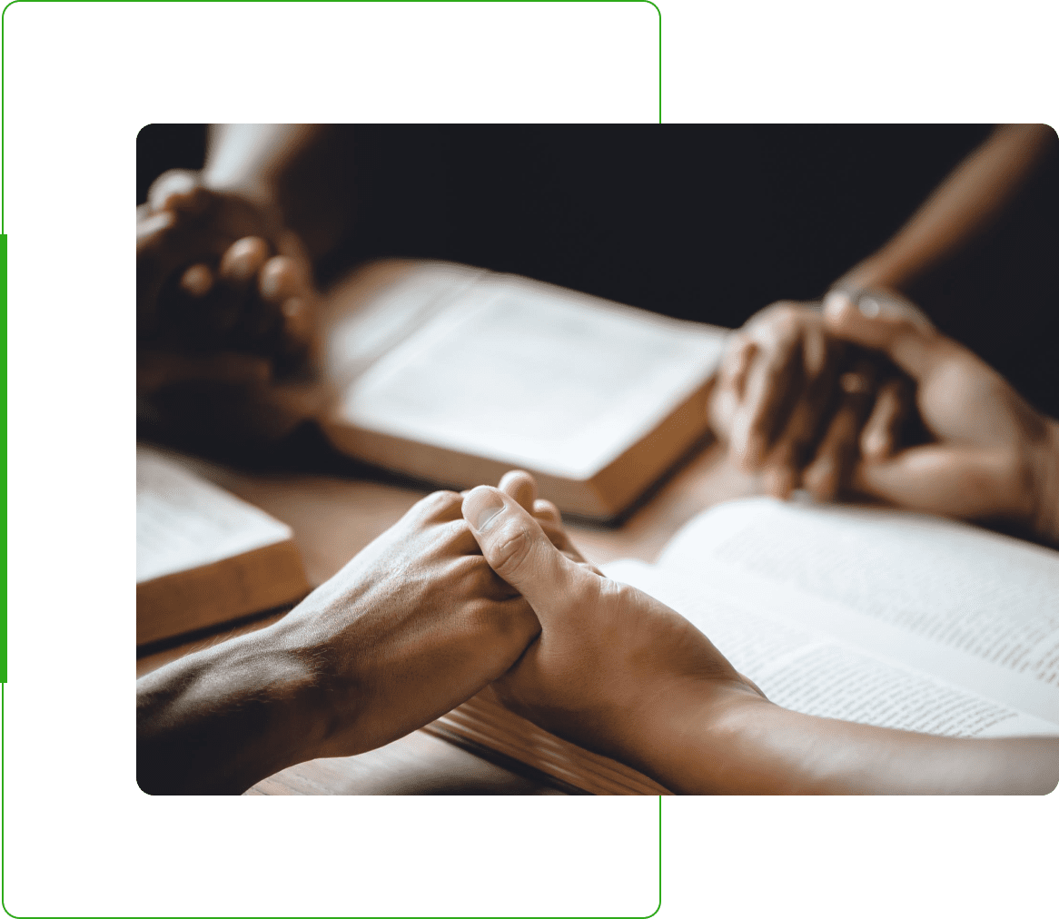 People holding hands in prayer over an open book on a table.
